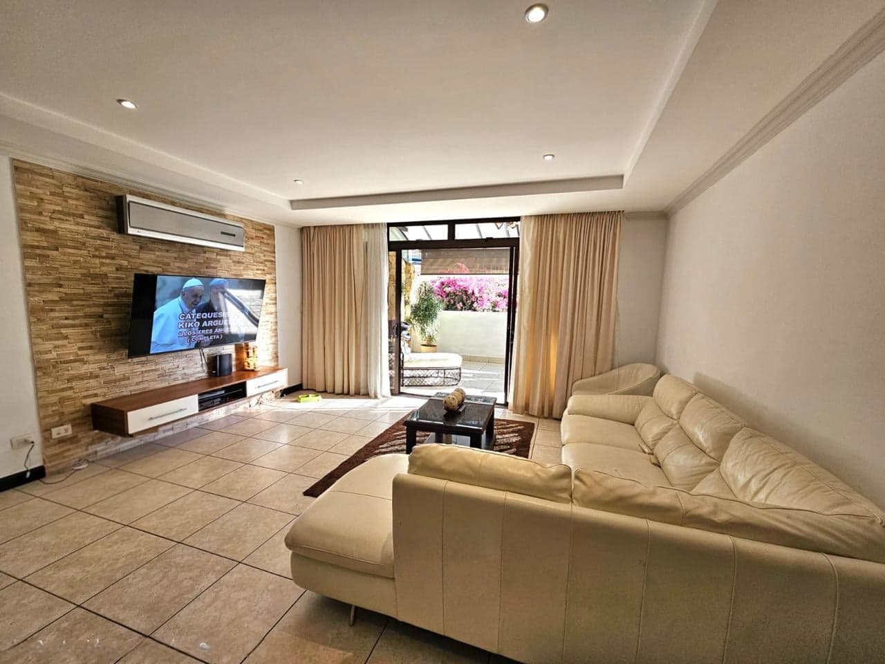 Sala con pared de piedra, televisión y salida a la terraza