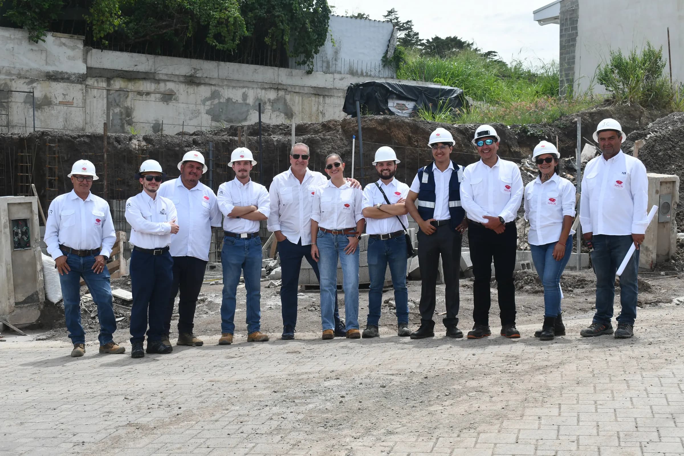 Once integrantes del equipo de Grupo Avalon, con cascos y camisas del grupo, frente a una obra en construcción