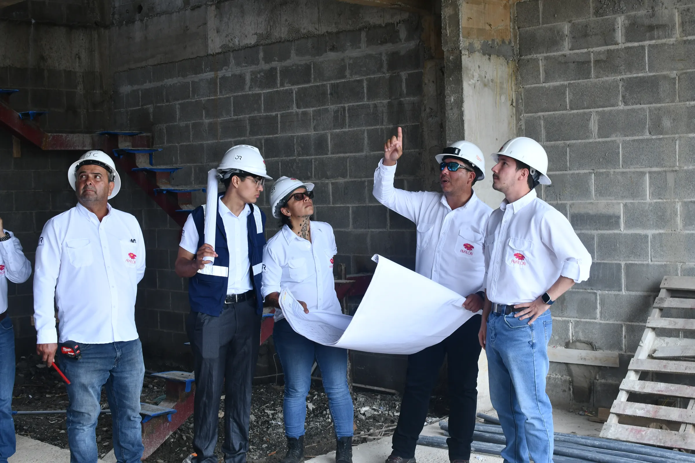 Integrantes del equipo de Grupo Avalon revisan un plano dentro de una obra en construcción; uno de ellos señala hacia arriba